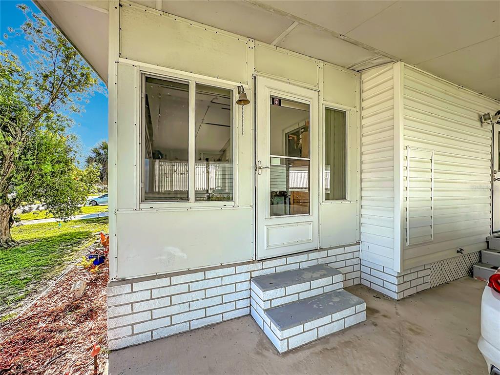 A white mobile home entrance features a screen door, a window, and brick-patterned steps — 8227 CINNAMON LANE, PORT ST LUCIE, FL