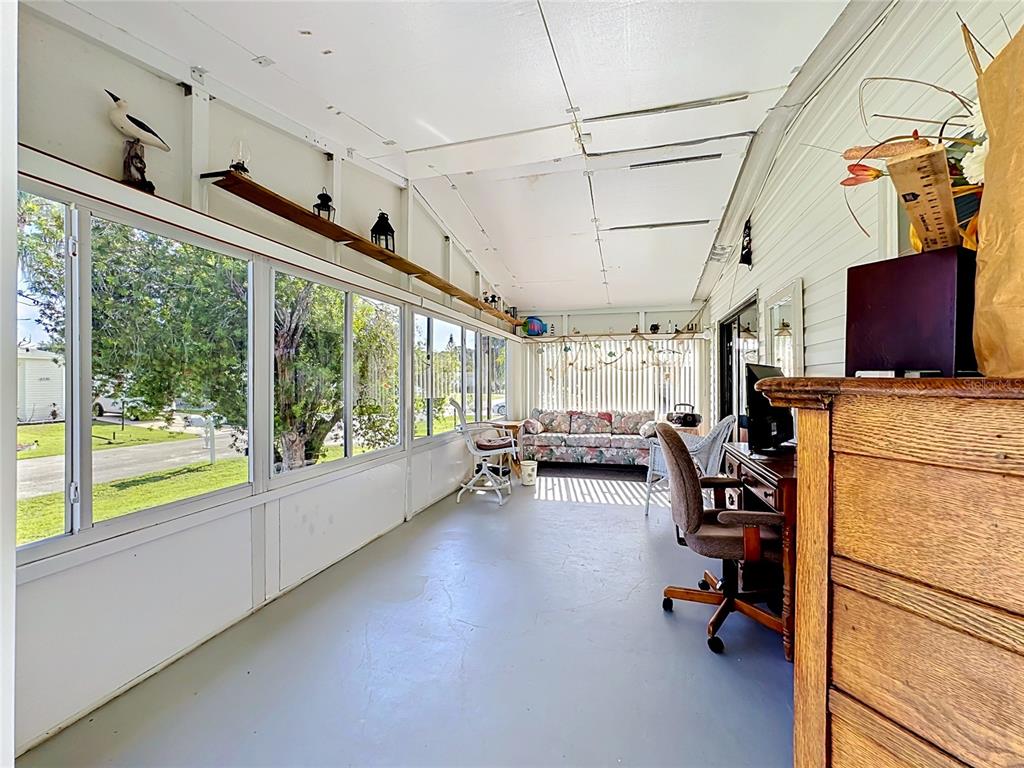A sunroom features large windows, a gray floor, a desk, and a floral sofa — 8227 CINNAMON LANE, PORT ST LUCIE, FL