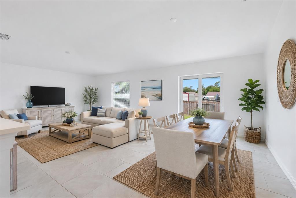 An open-concept living and dining area features light tile flooring, neutral furniture, and area rugs — 1403 AKEN STREET, PORT CHARLOTTE, FL