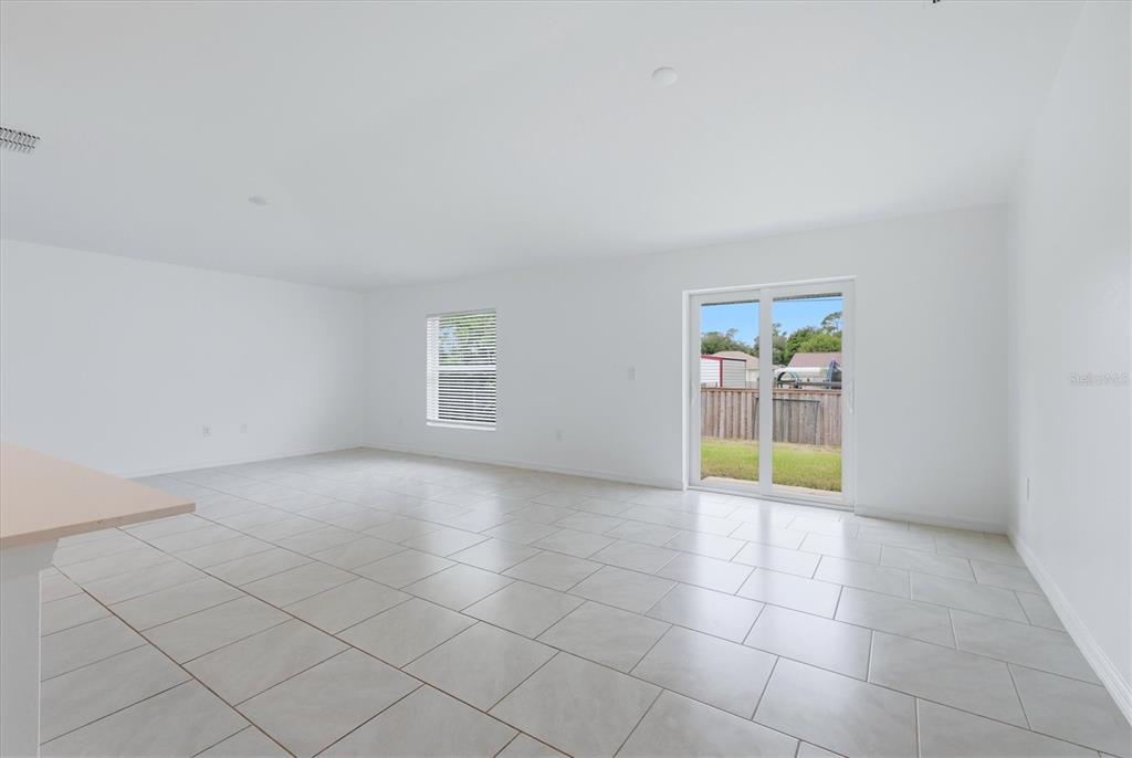 An empty room with white walls, light-colored tile flooring, a window, and sliding glass doors — 1403 AKEN STREET, PORT CHARLOTTE, FL
