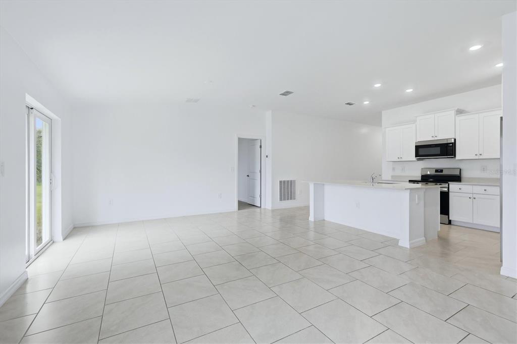 An open-concept kitchen and living area features white cabinetry, stainless steel appliances, and tile flooring — 1403 AKEN STREET, PORT CHARLOTTE, FL