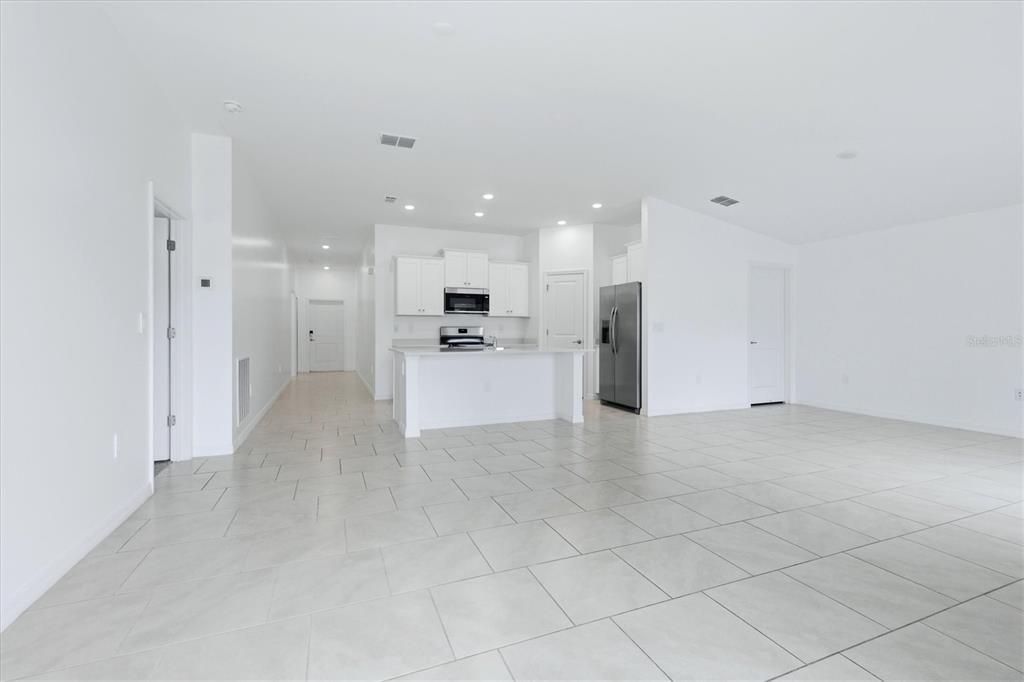 A bright, open-concept kitchen and living area features white cabinetry, stainless appliances, and tile flooring — 1403 AKEN STREET, PORT CHARLOTTE, FL