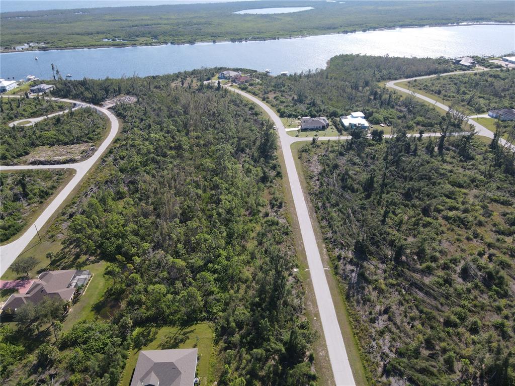 An aerial view shows a paved road winding through a wooded area near a waterway — 16042 LANKFORD COURT, PORT CHARLOTTE, FL