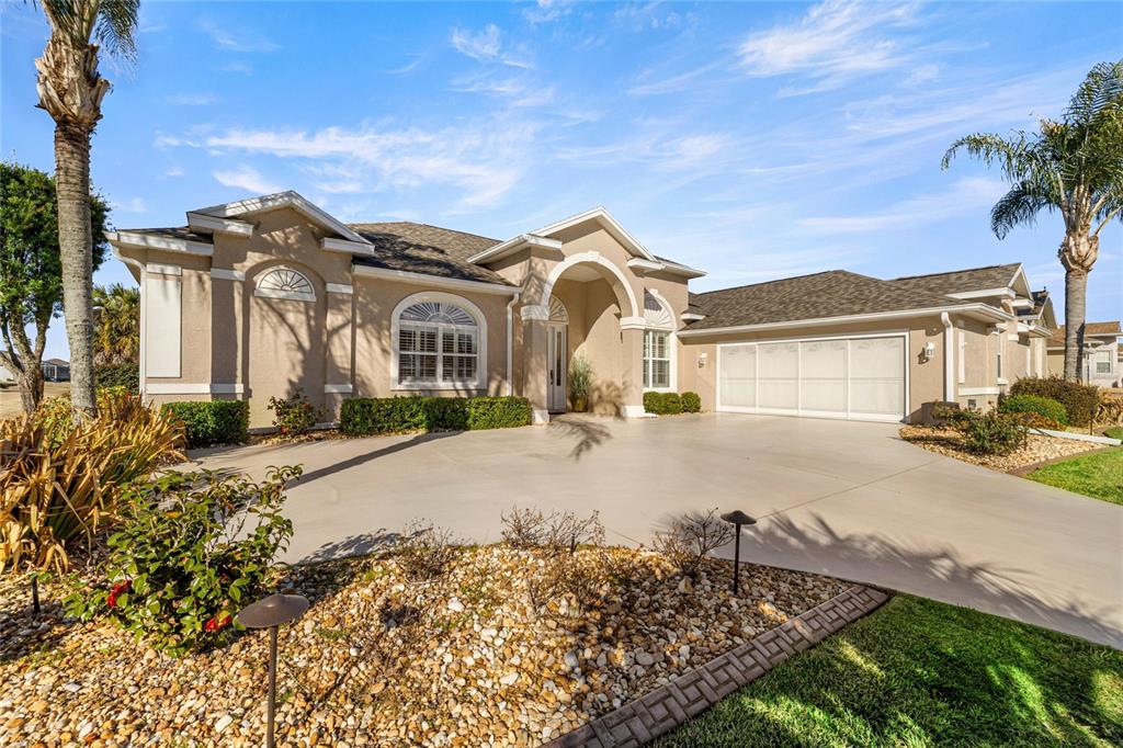 A single-story beige house with a large concrete driveway, arched entryway, and palm trees — 5801 NW 18TH STREET, OCALA, FL