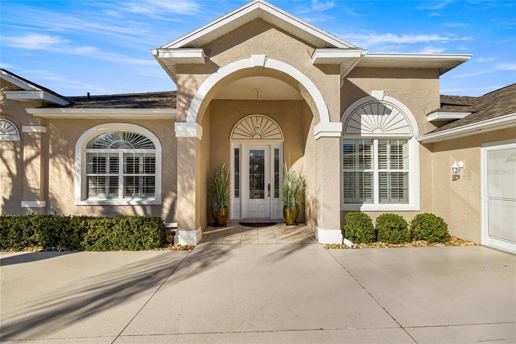 The exterior of a beige stucco house features a covered entryway and arched windows — 5801 NW 18TH STREET, OCALA, FL