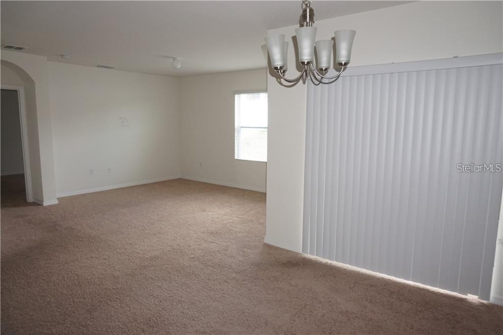 An empty room with beige carpet, white walls, a chandelier, and vertical window blinds — 119 BELLA DRIVE, DAVENPORT, FL