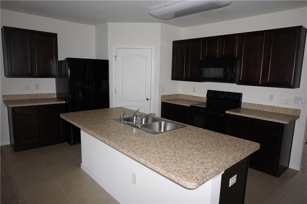 A kitchen features dark wood cabinets, tan laminate countertops, black appliances, and a central island — 119 BELLA DRIVE, DAVENPORT, FL