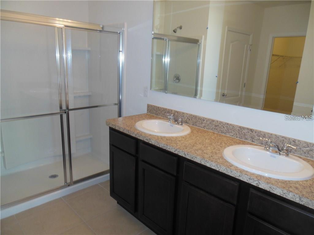 A bathroom features a double vanity with dark cabinets, granite countertops, and a glass-enclosed shower — 119 BELLA DRIVE, DAVENPORT, FL