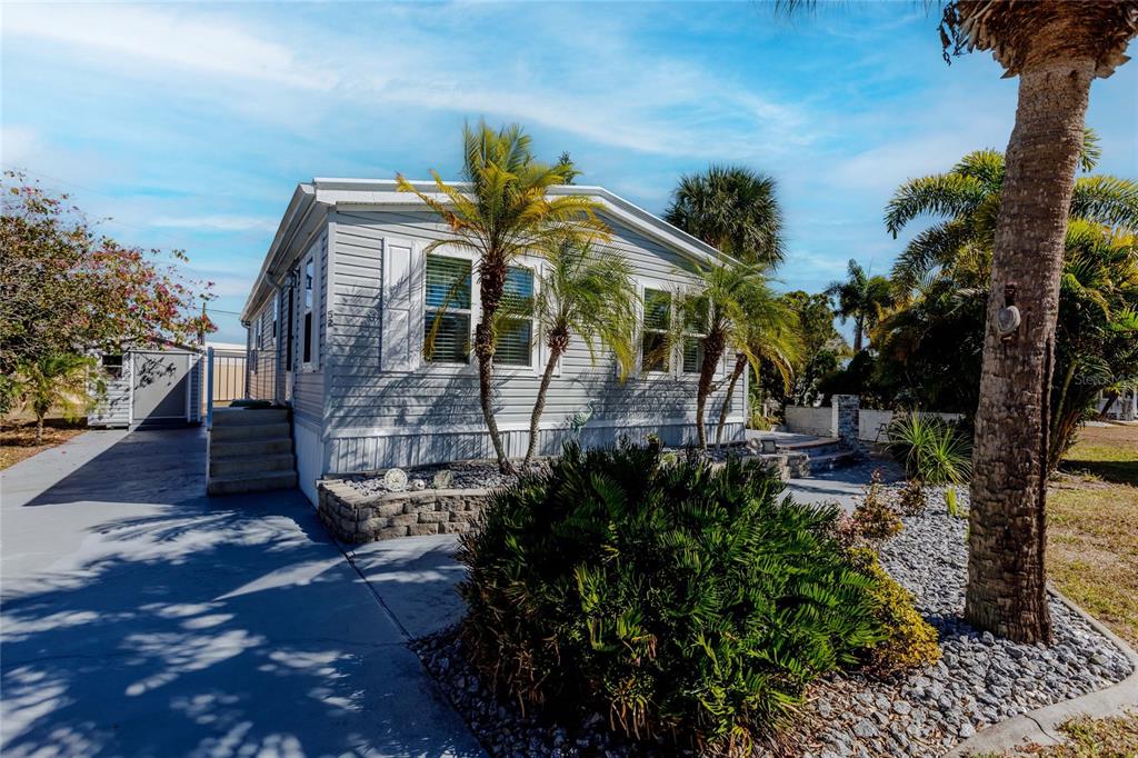 A light gray manufactured home features a concrete driveway, palm trees, and a small shed — 2100 KINGS HIGHWAY UNIT 52, PORT CHARLOTTE, FL