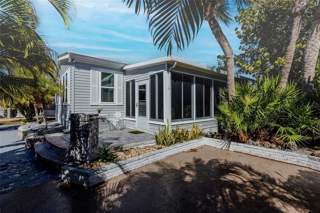 A light gray manufactured home features a screened-in porch, a stone patio, and palm trees — 2100 KINGS HIGHWAY UNIT 52, PORT CHARLOTTE, FL