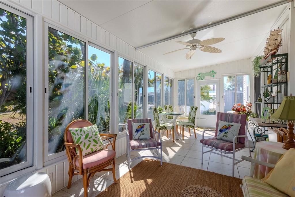 A sunroom with tile floors, a ceiling fan, and large windows overlooking tropical greenery — 2100 KINGS HIGHWAY UNIT 52, PORT CHARLOTTE, FL