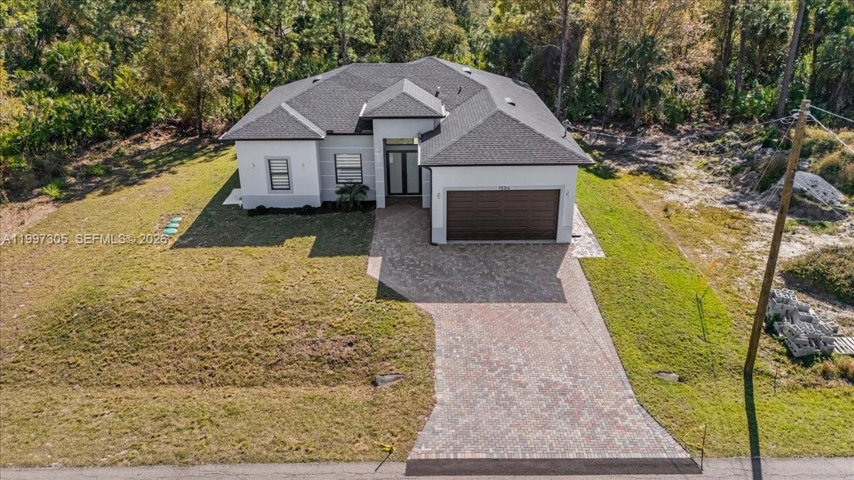 An aerial view shows a single-story house with a paved driveway and a two-car garage — 1504 E 6th, Lehigh Acres FL 33972, LEHIGH ACRES, FL