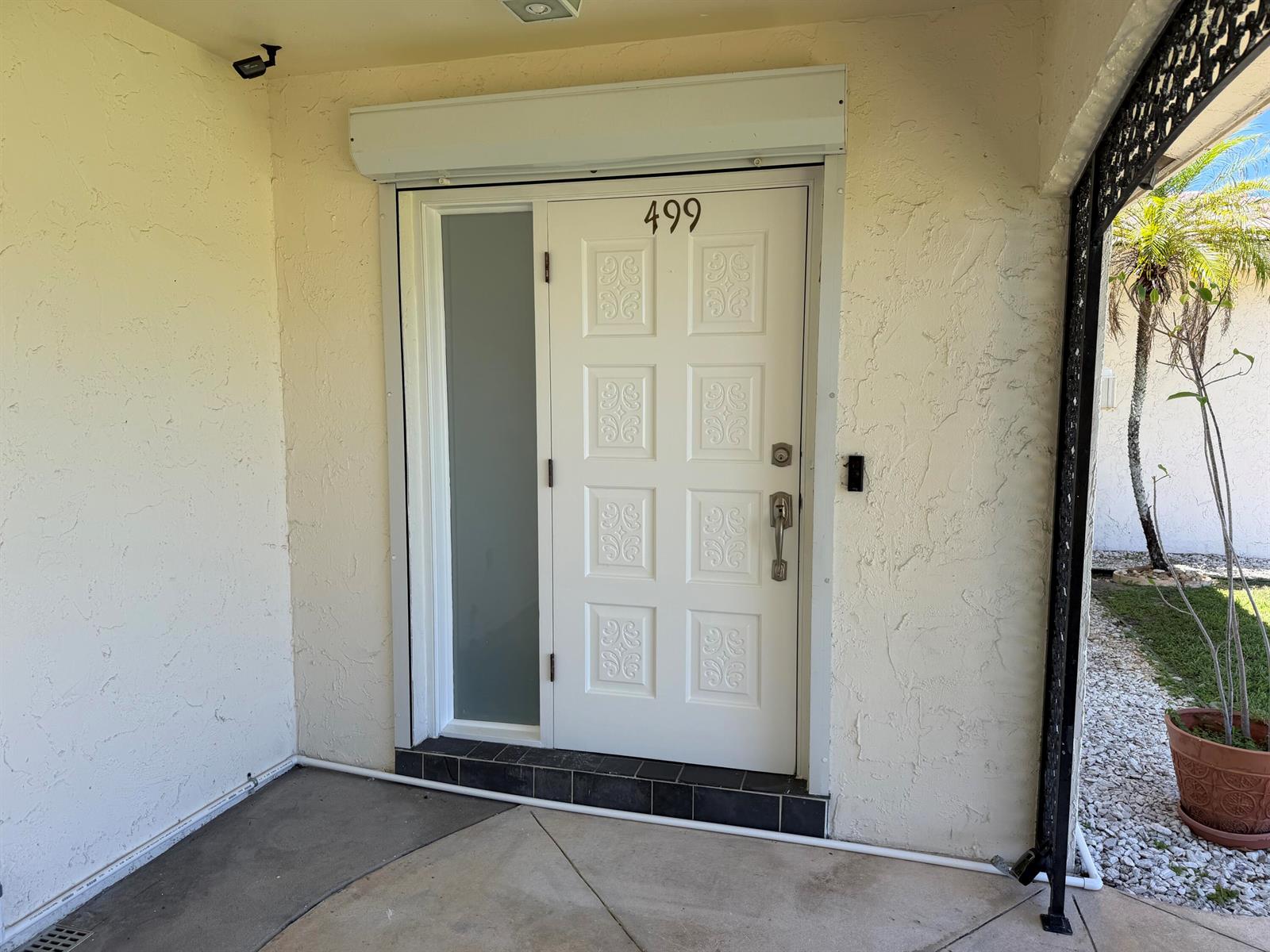 A white front door with a frosted glass sidelight sits under a roll-down security shutter — 499 W Conference Drive, Boca Raton FL 33486, BOCA RATON, FL