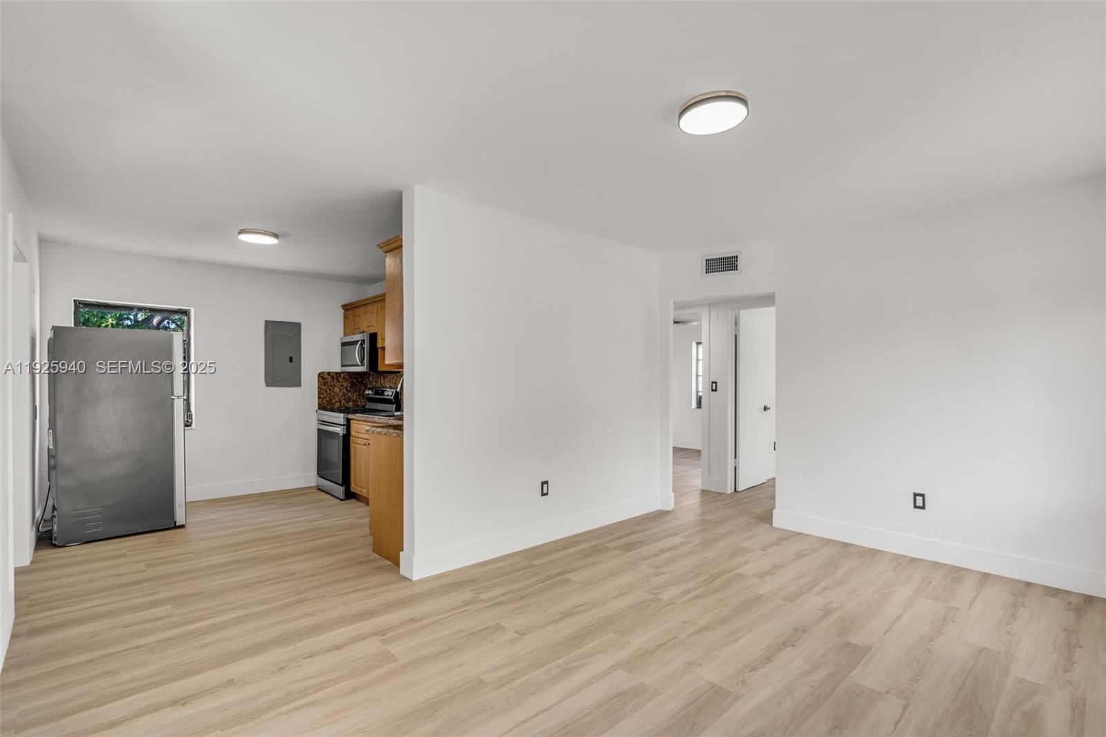 A bright living area with light wood-look flooring leads into a small kitchen — 739 W 30th St, Hialeah FL 33012, HIALEAH, FL