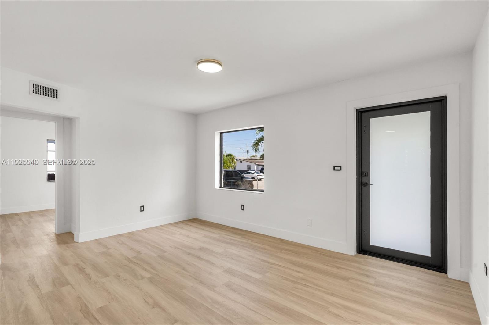 A minimalist room features light wood-look flooring, white walls, a window, and a glass door — 739 W 30th St, Hialeah FL 33012, HIALEAH, FL