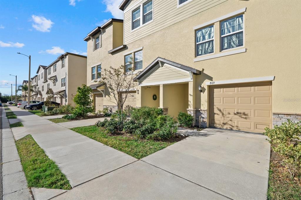 A multi-story townhouse exterior with a tan facade, a single-car garage, and a concrete driveway — 809 TENNYSON MILL CIRCLE, TAMPA, FL