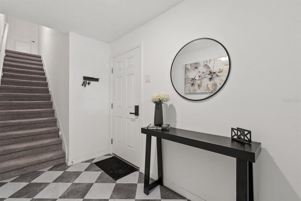 An entryway features a staircase, a black console table, a round mirror, and checkered flooring — 809 TENNYSON MILL CIRCLE, TAMPA, FL