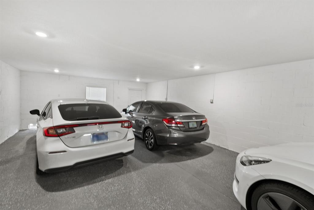 A spacious garage with white block walls, recessed lighting, and three parked cars — 809 TENNYSON MILL CIRCLE, TAMPA, FL