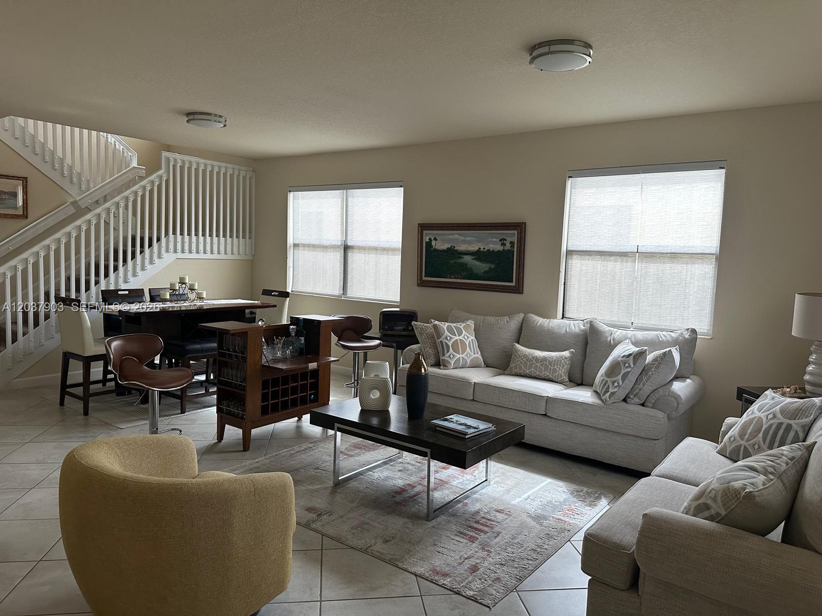 A living room features a staircase, dining area, bar, and neutral-toned furniture on tile floors — HOMESTEAD, FL