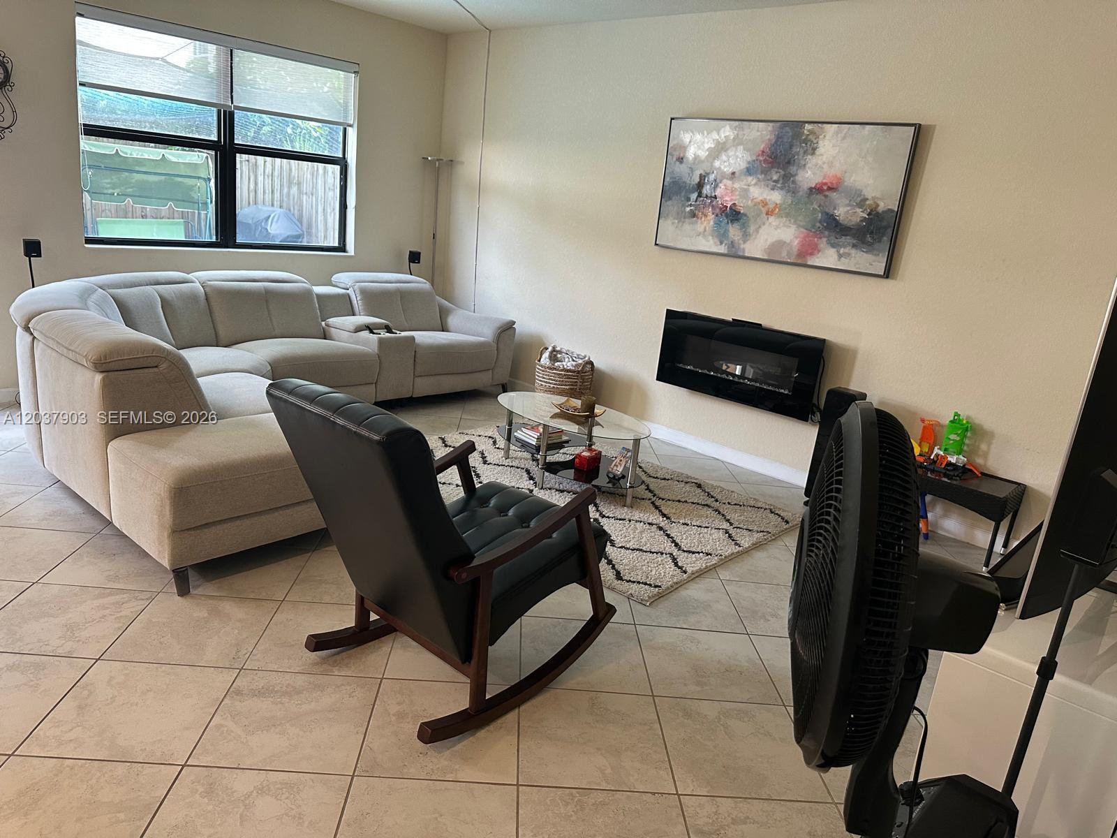 A living room features a light-colored sectional sofa, a black rocking chair, and a fireplace — HOMESTEAD, FL
