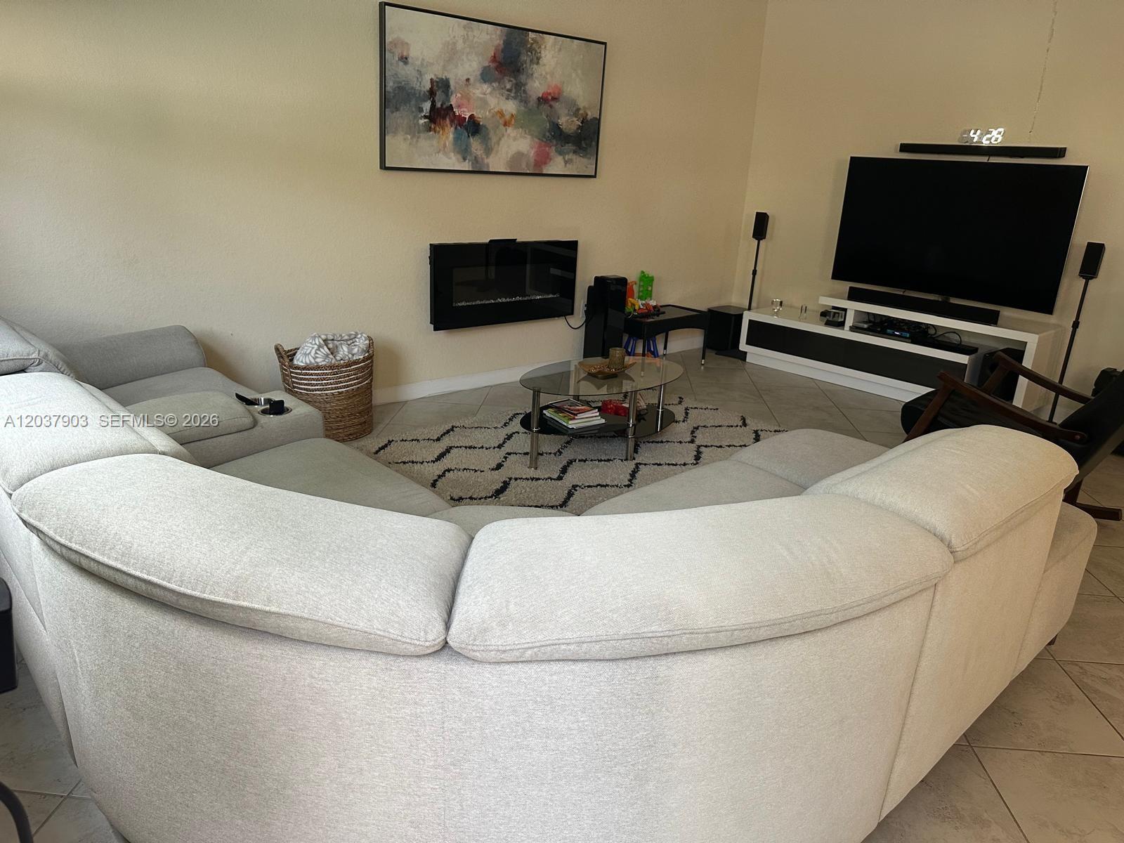 A living room features a large curved sectional sofa, a fireplace, and a television console — HOMESTEAD, FL