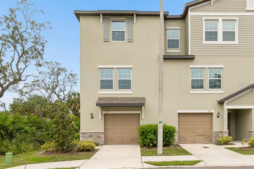 An aerial view shows multi-story residential buildings surrounded by dense trees and a nearby bay — 873 TENNYSON MILL CIRCLE, TAMPA, FL