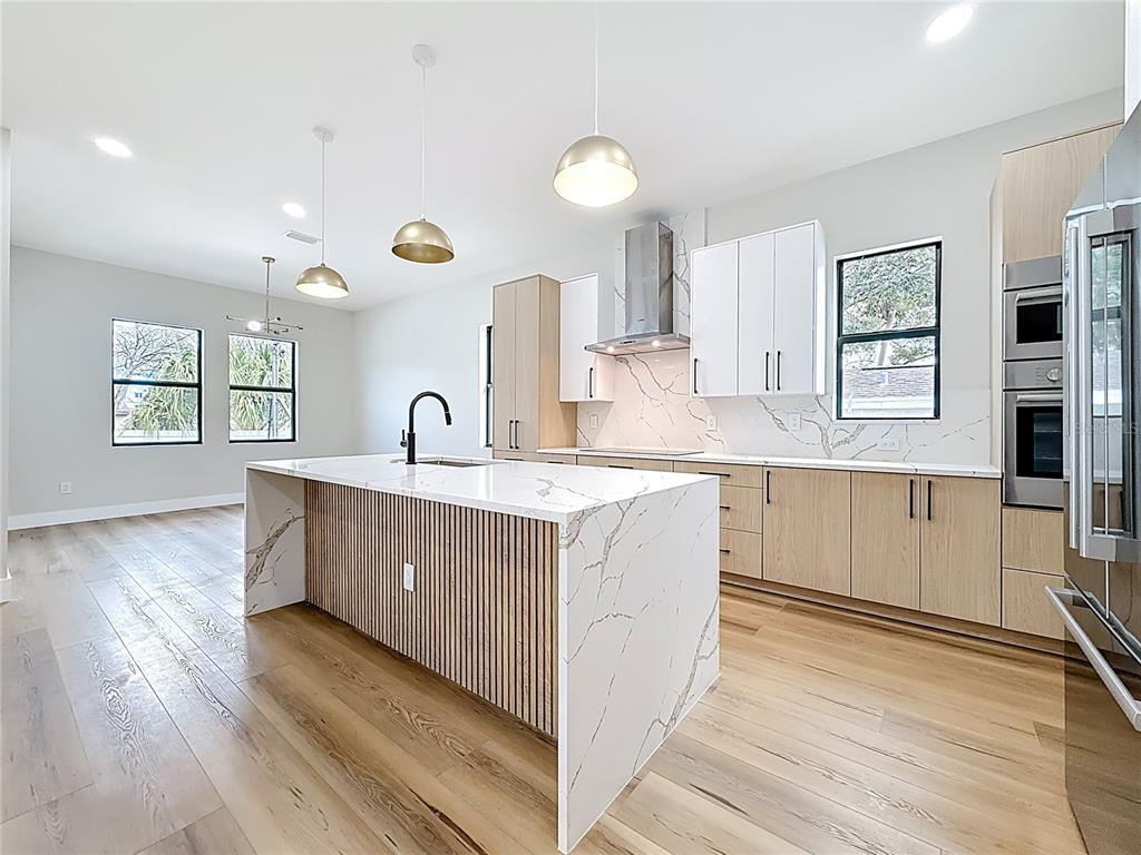A modern kitchen features a marble waterfall island, light wood cabinetry, and white upper cabinets — 4219 W BAY VIEW AVENUE, TAMPA, FL