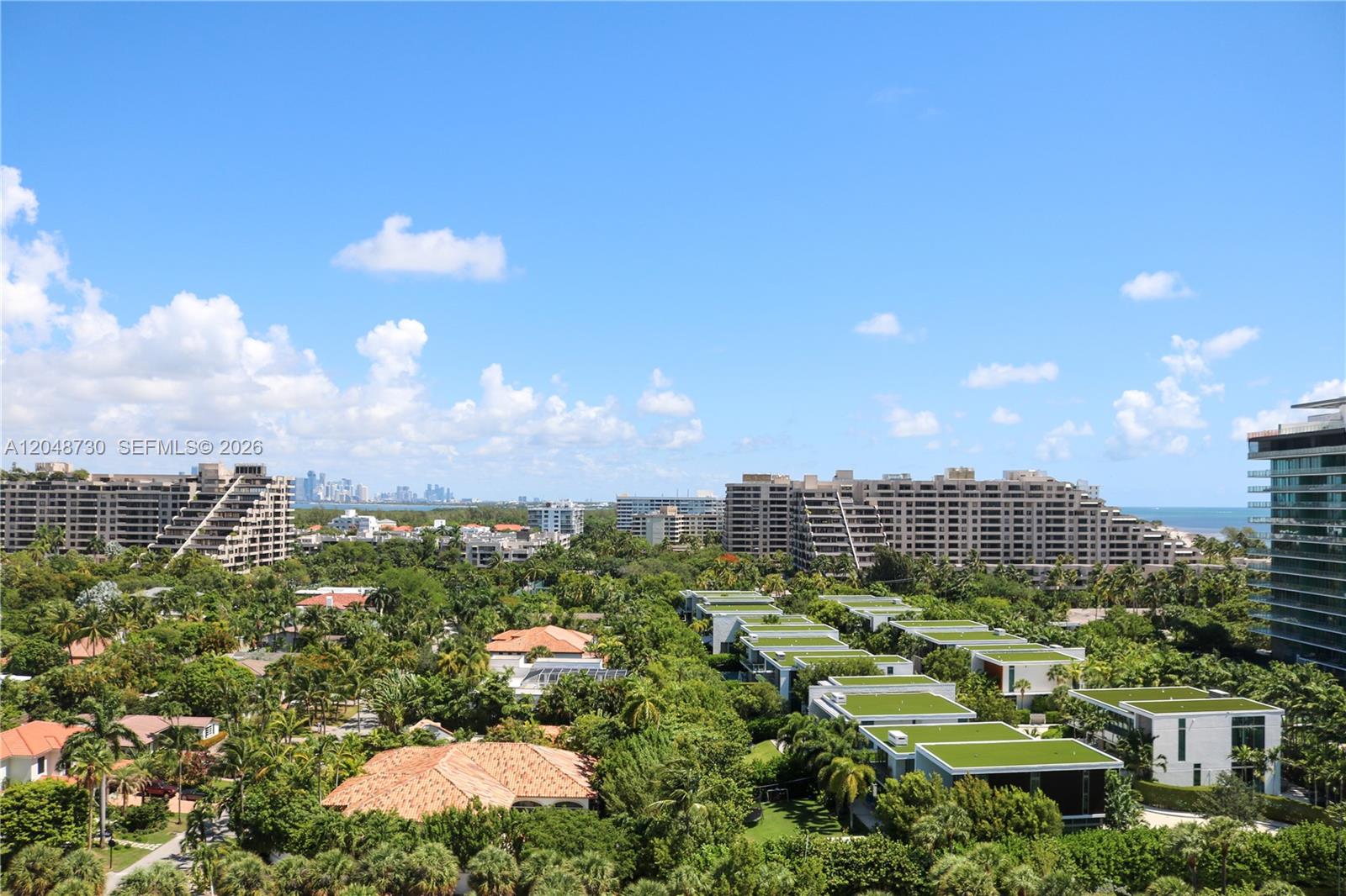 An elevated view shows residential buildings surrounded by lush trees under a blue sky — KEY BISCAYNE, FL