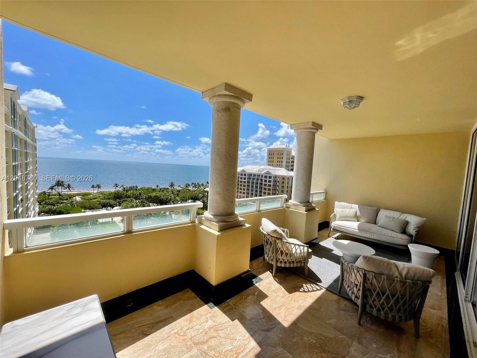 A covered balcony features stone columns, tile flooring, outdoor furniture, and a view of the ocean — KEY BISCAYNE, FL