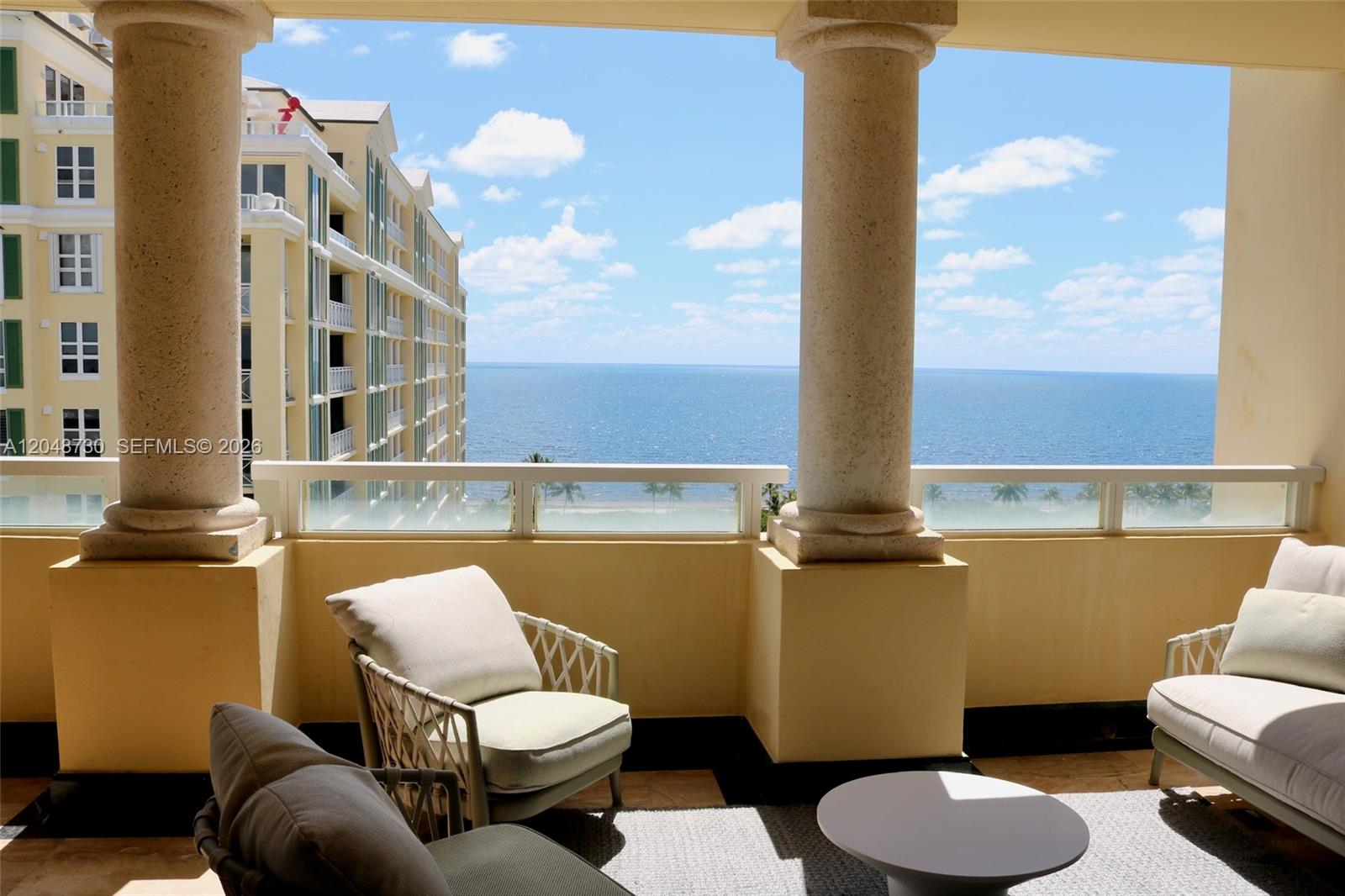 A balcony with stone columns overlooks the ocean and a neighboring building — KEY BISCAYNE, FL