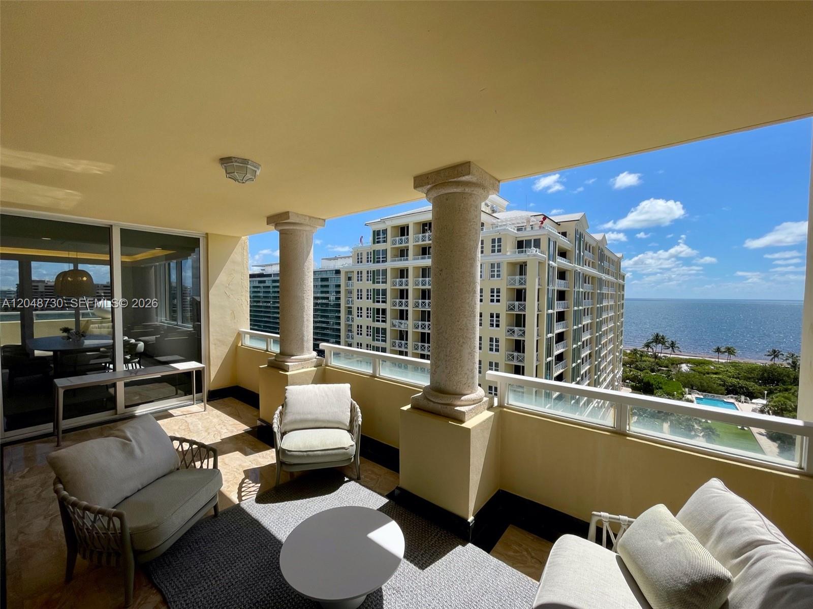 A balcony with outdoor furniture, stone columns, and a view of the ocean and buildings — KEY BISCAYNE, FL