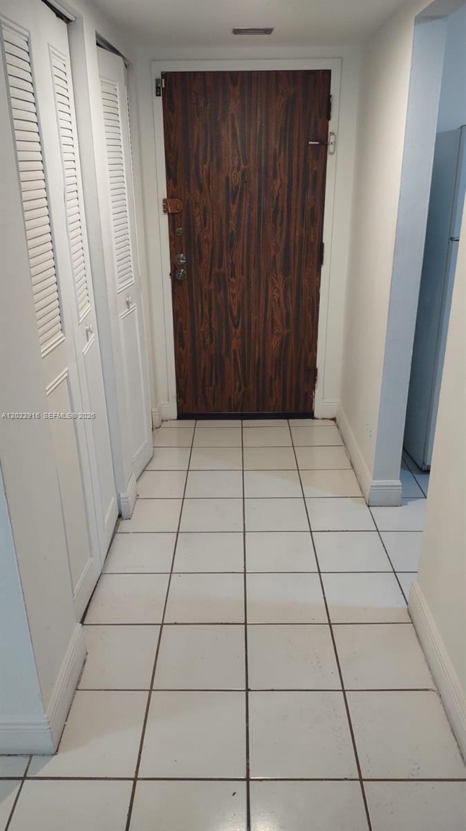 A hallway with white tiled floors leads to a wood-grain door and louvered closet doors — 496 NW 165th St Rd # D109, Miami FL 33169, MIAMI, FL