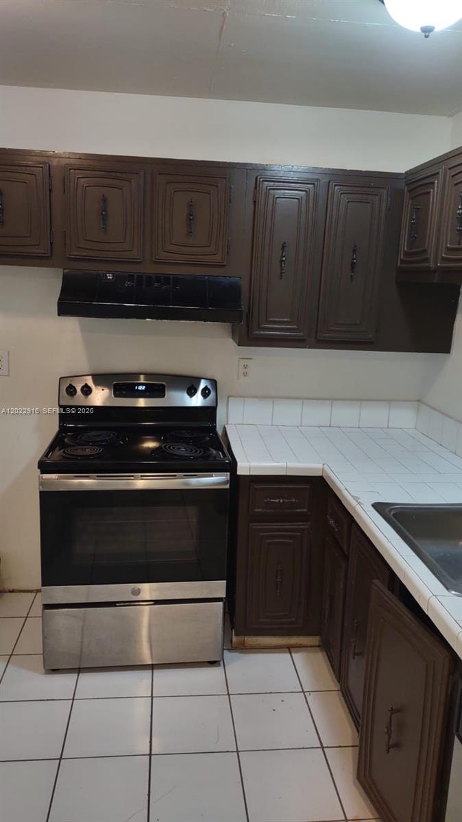 A kitchen features dark brown cabinets, a stainless steel stove, and white tiled countertops — 496 NW 165th St Rd # D109, Miami FL 33169, MIAMI, FL