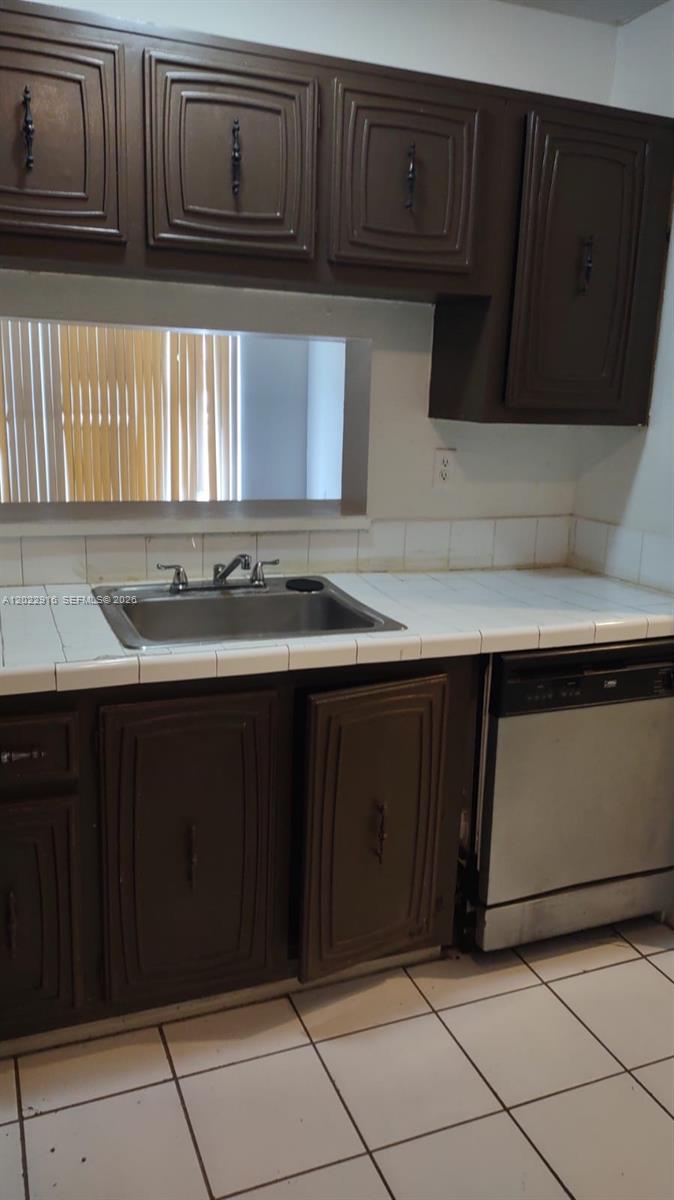 A kitchen features dark brown cabinets, a stainless steel sink, and white tiled countertops — 496 NW 165th St Rd # D109, Miami FL 33169, MIAMI, FL