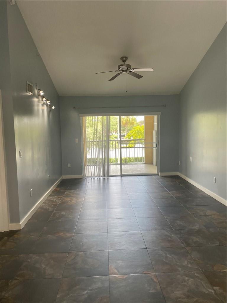 An empty living room features blue walls, dark tile flooring, a ceiling fan, and sliding doors — 2640 S University Drive # 319, Davie FL 33328, DAVIE, FL