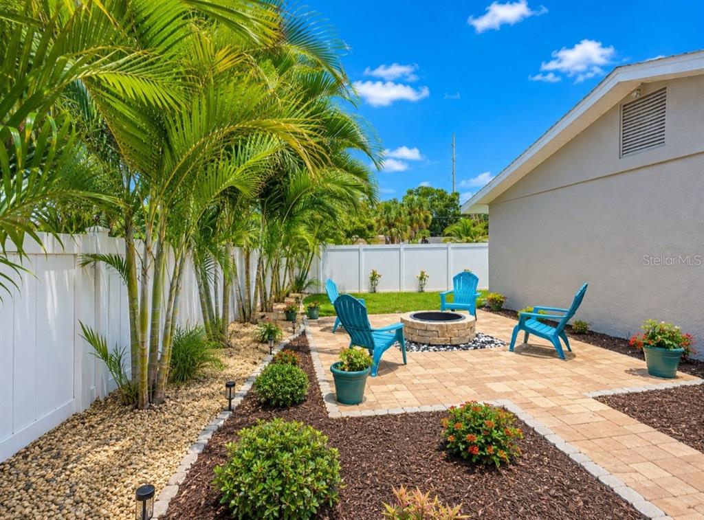 A backyard patio features a stone fire pit, blue Adirondack chairs, and palm trees — 138 DAVISON AVENUE NE, ST PETERSBURG, FL