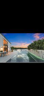 An infinity pool overlooks a river at sunset next to a modern house with patio — 6110 N Ocean Boulevard # 39, Ocean Ridge FL 33435, OCEAN RIDGE, FL