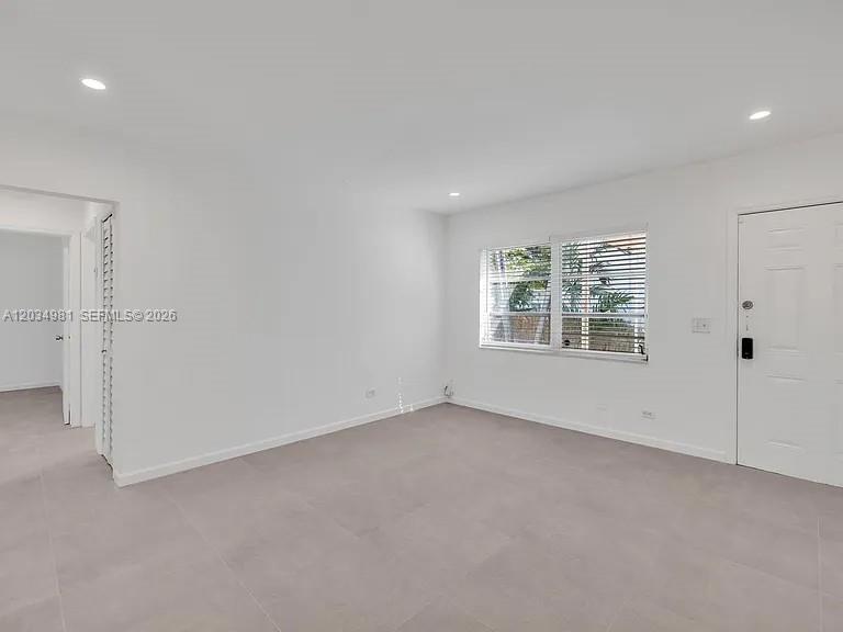An empty room features white walls, light-colored tile flooring, a window with blinds, and a door — 545 NE 64th St, Miami FL 33138, MIAMI, FL