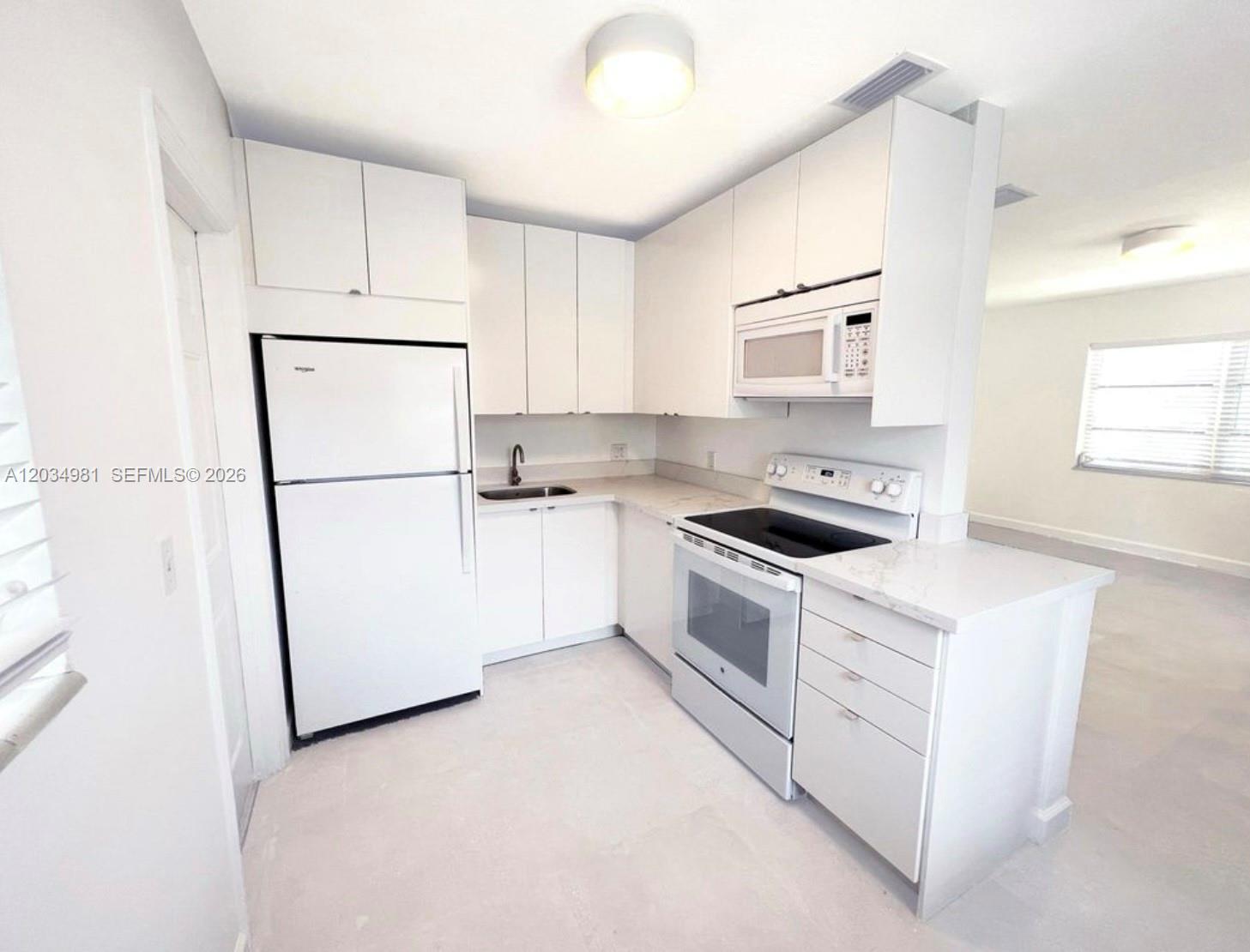 A white kitchen features white cabinetry, stainless steel appliances, and light-colored countertops — 545 NE 64th St, Miami FL 33138, MIAMI, FL