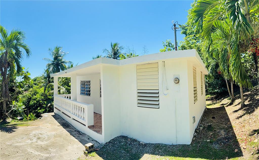 A white, single-story house with a covered porch and louvered windows sits on a hillside — KM 5.0 906, YABUCOA, PR