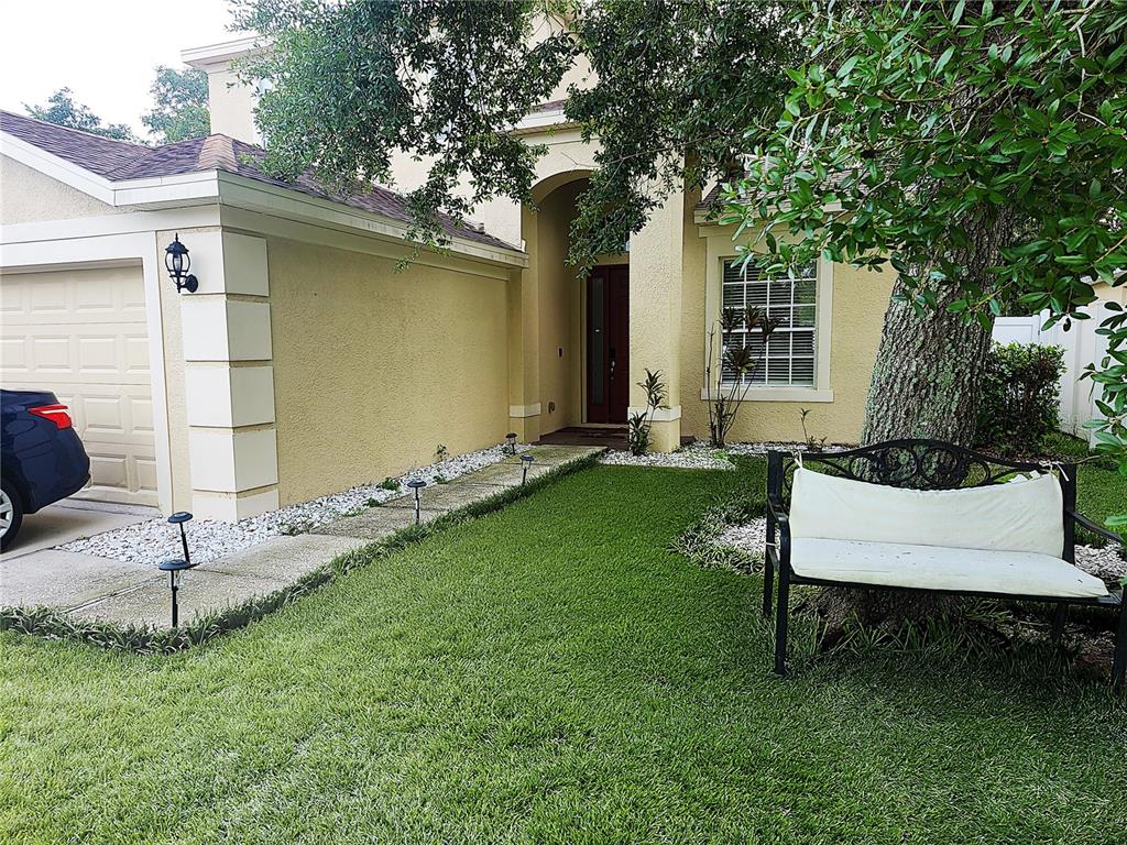 A beige house exterior features a garage, a front walkway, and a bench under a tree — 8604 TIDAL BREEZE DRIVE, RIVERVIEW, FL