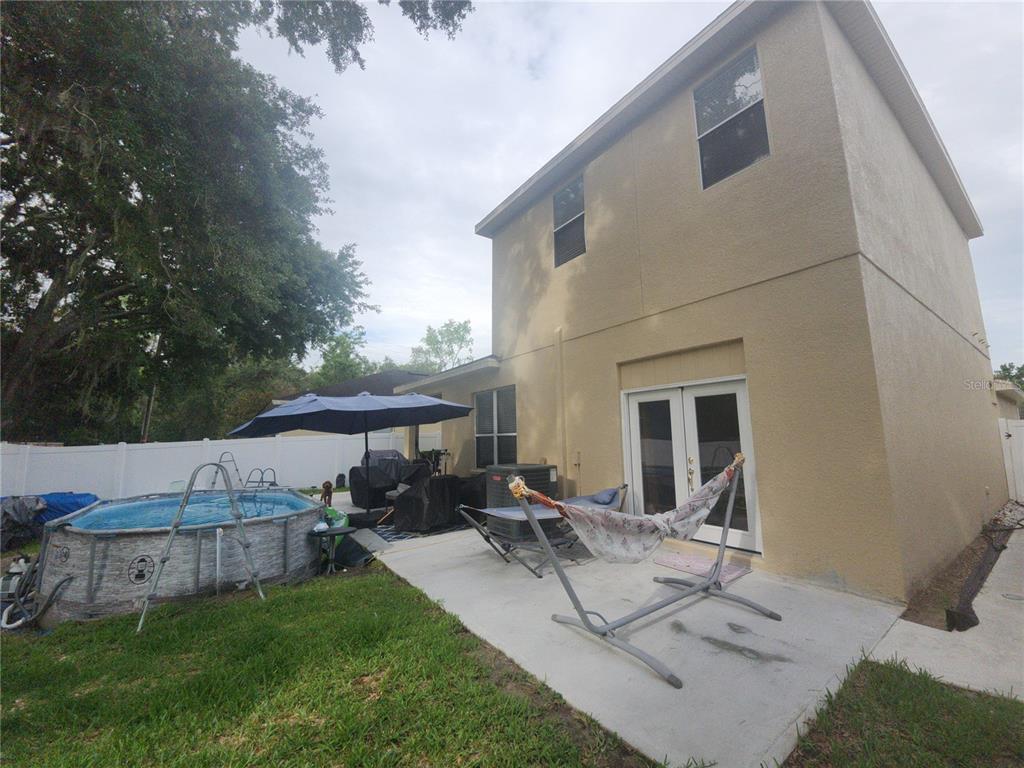 A backyard features a concrete patio, an above-ground pool, a hammock, and a two-story house — 8604 TIDAL BREEZE DRIVE, RIVERVIEW, FL