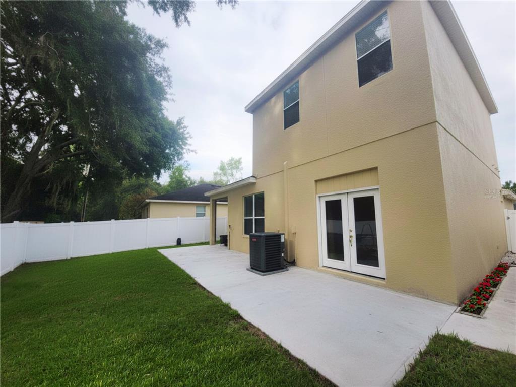 A two-story house exterior with a concrete patio, white vinyl fence, and green lawn — 8604 TIDAL BREEZE DRIVE, RIVERVIEW, FL