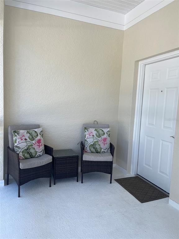 A covered patio features two wicker chairs with floral pillows and a small side table — 3706 54TH DRIVE W UNIT 204, BRADENTON, FL