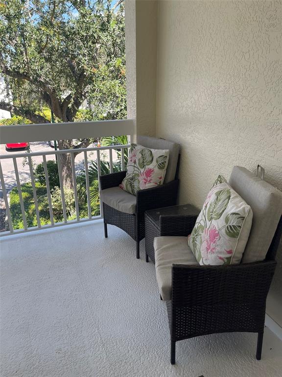 A balcony features two wicker chairs with floral cushions and a small side table — 3706 54TH DRIVE W UNIT 204, BRADENTON, FL