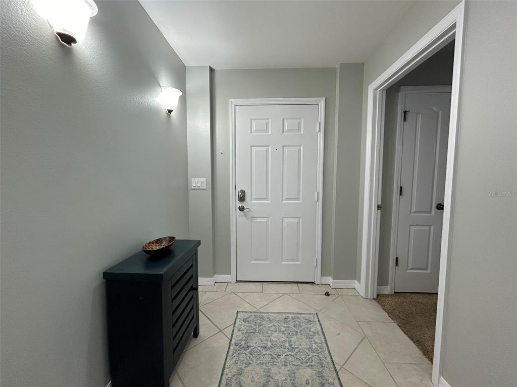 An entryway features light gray walls, tile flooring, a white front door, and a dark cabinet — 3706 54TH DRIVE W UNIT 204, BRADENTON, FL