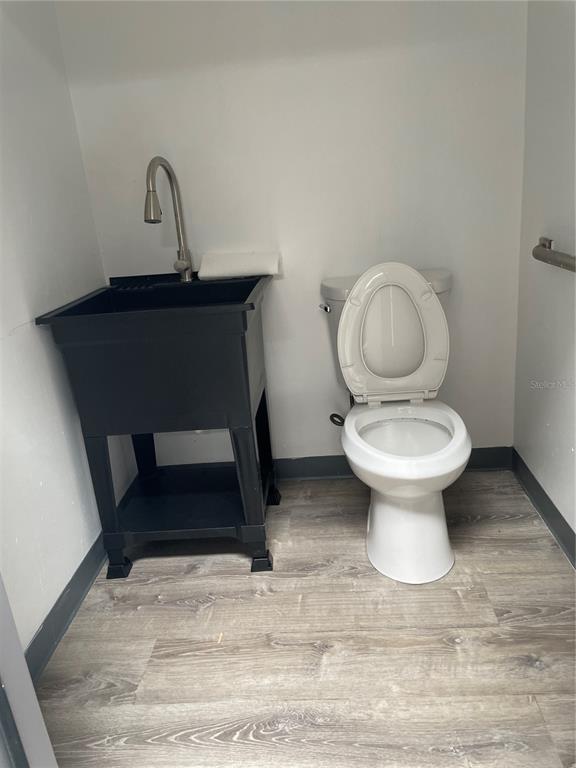 A small bathroom features a utility sink, a white toilet, and wood-look flooring — 5525 COMMERCE DRIVE UNIT 3/4, ORLANDO, FL