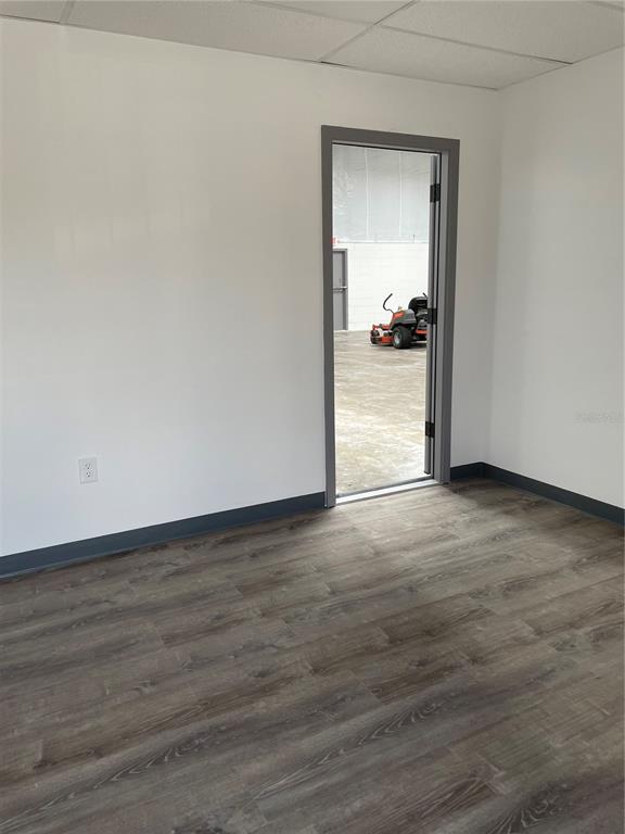 An empty room with wood-look flooring and a doorway leading to a warehouse space — 5525 COMMERCE DRIVE UNIT 3/4, ORLANDO, FL