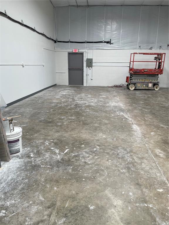 An empty warehouse space features a concrete floor, white walls, an exit door, and equipment — 5525 COMMERCE DRIVE UNIT 3/4, ORLANDO, FL
