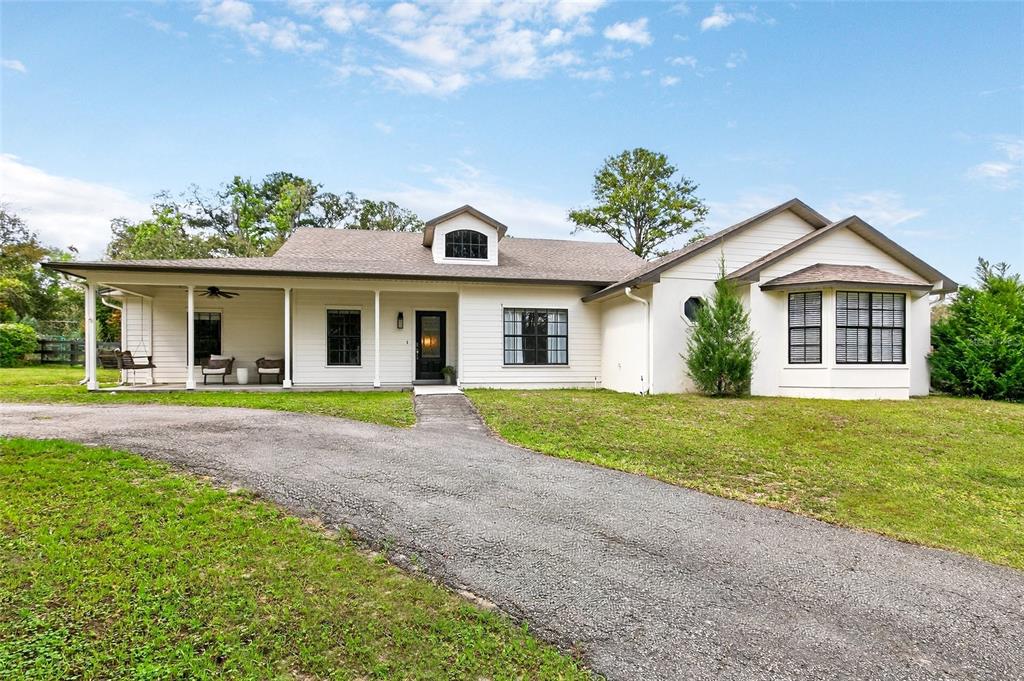 A single-story house with white siding, a covered porch, and a paved driveway — 22301 CORONADO SOMERSET DRIVE, SORRENTO, FL
